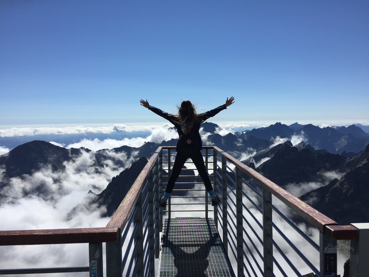 γυναίκα που σηκώνει τα χέρια της ψηλά σε μία σιδερένια γέφυρα πάνω από βουνά